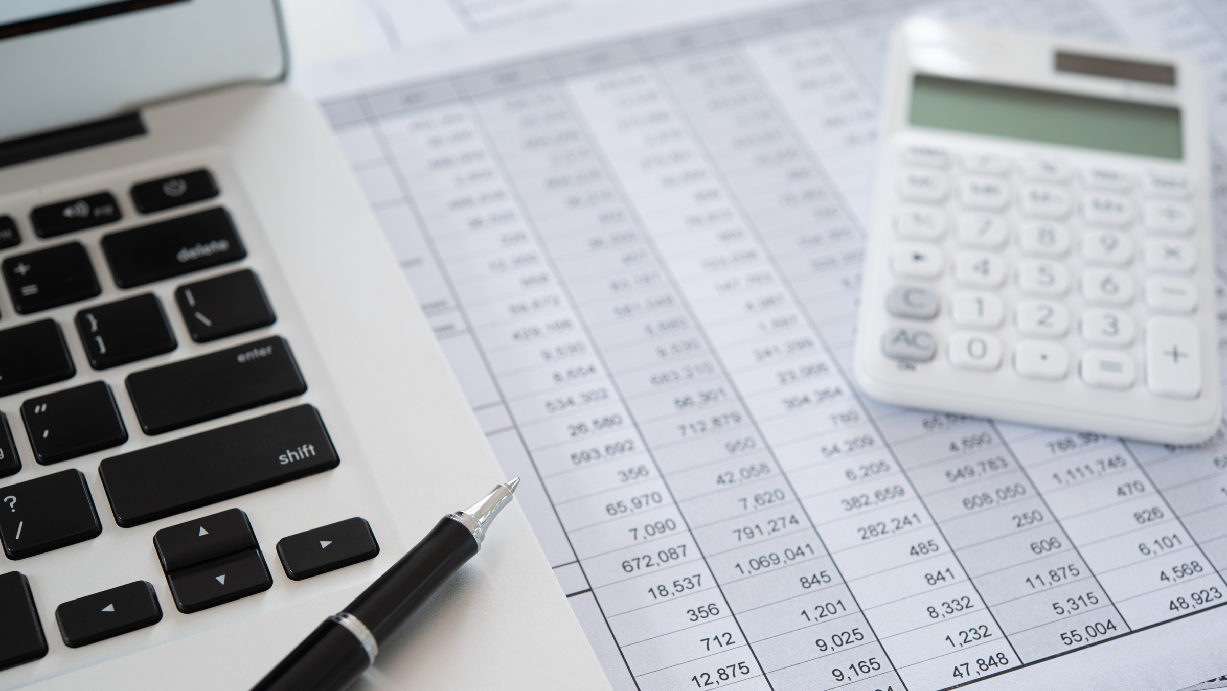 laptop, pen, and calculator atop a spreadsheet